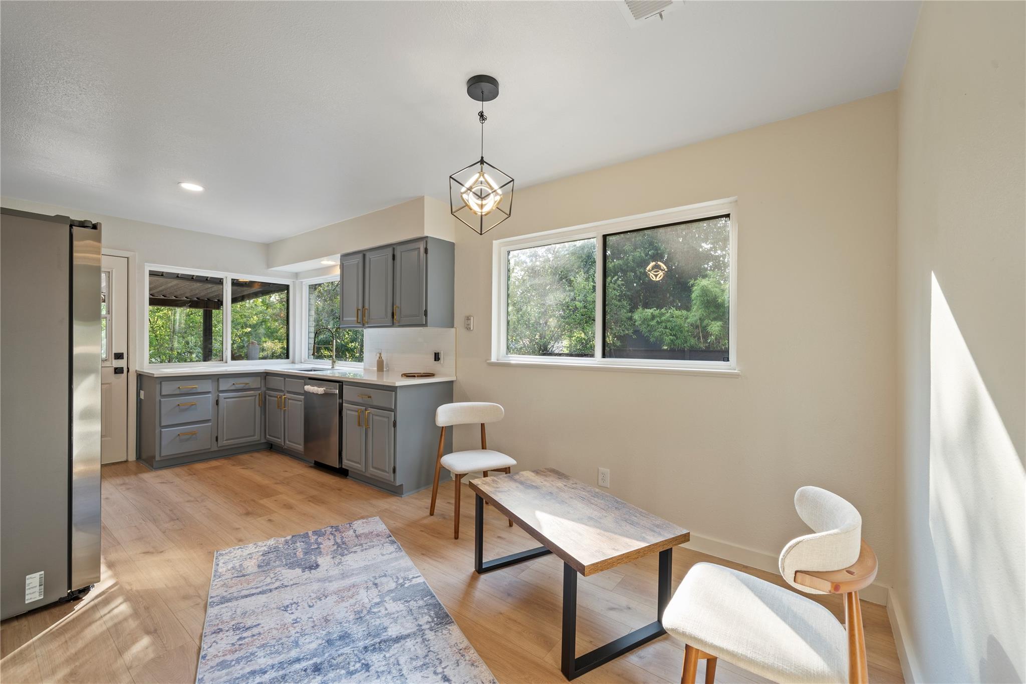 Kitchen and dining area with gray cabinetry, stainless appliances, and large windows overlooking greenery.
