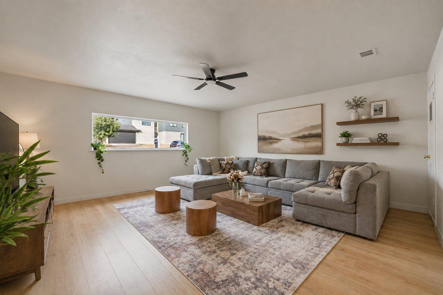 Staged living room with a gray sectional, patterned rug, wood tables, and wide horizontal window.
