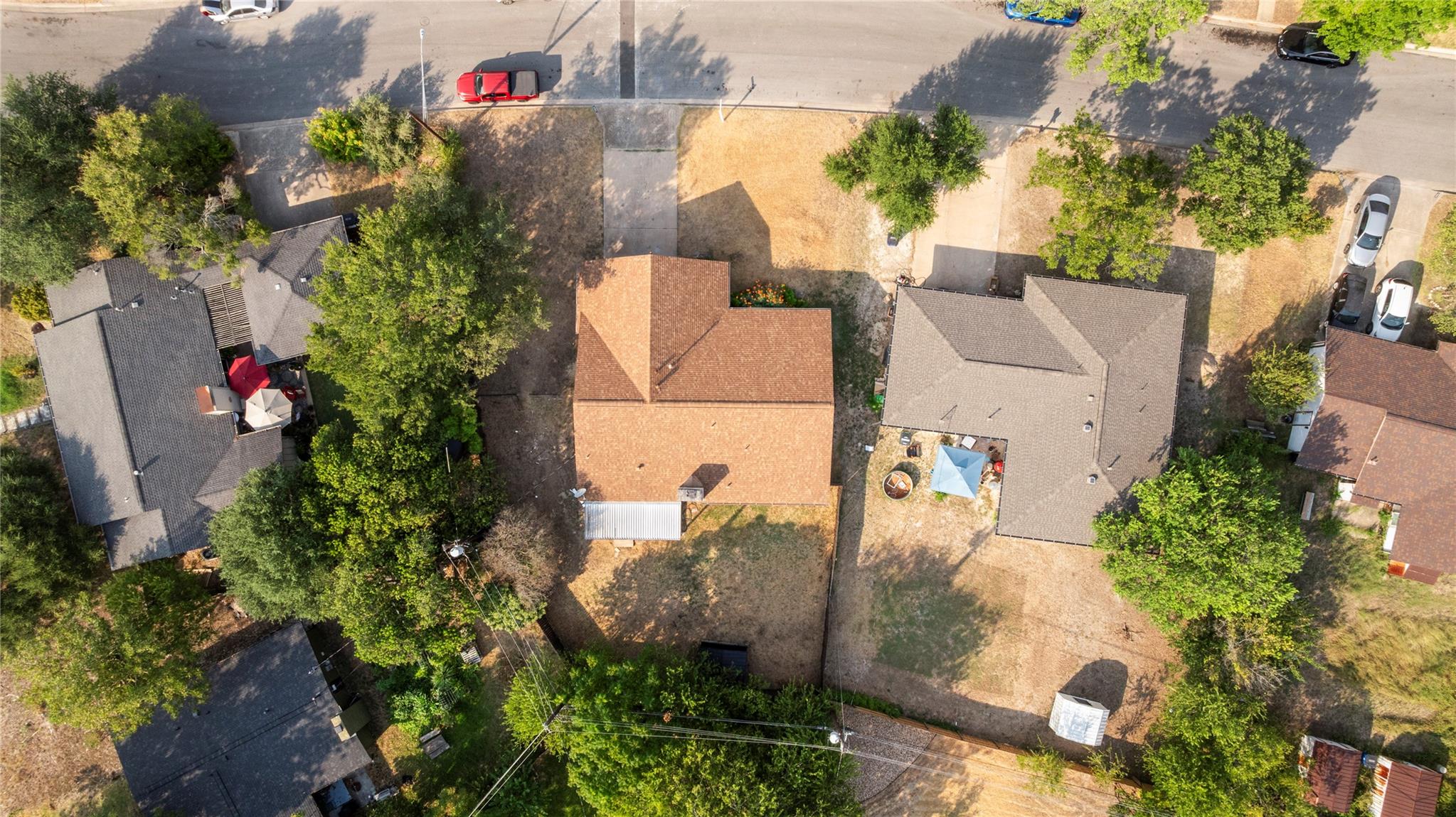 Aerial view of a reddish-brown-roofed house with a dry yard and mature trees.