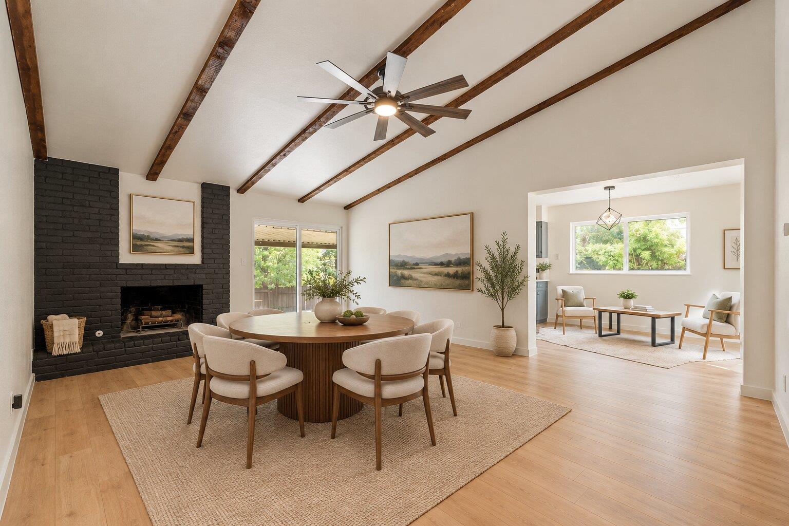 Open-plan dining room with a round table, black brick fireplace, and exposed wood ceiling beams.