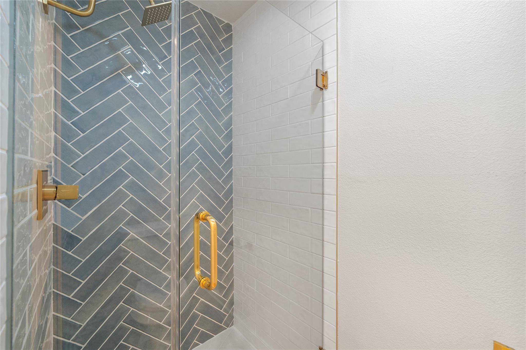 Glass shower with blue-gray herringbone tile and brass fixtures.