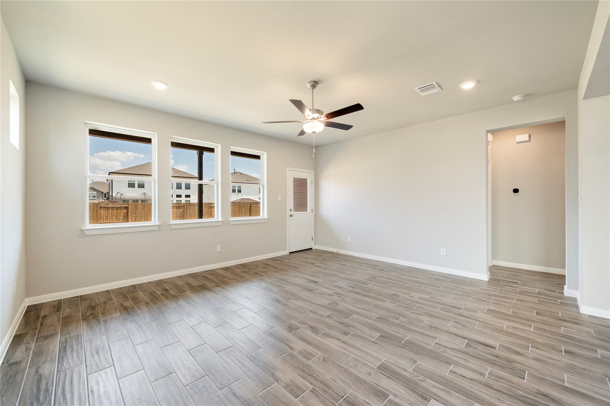 Vacant living area with wood-look tile floors, three windows, and a ceiling fan.