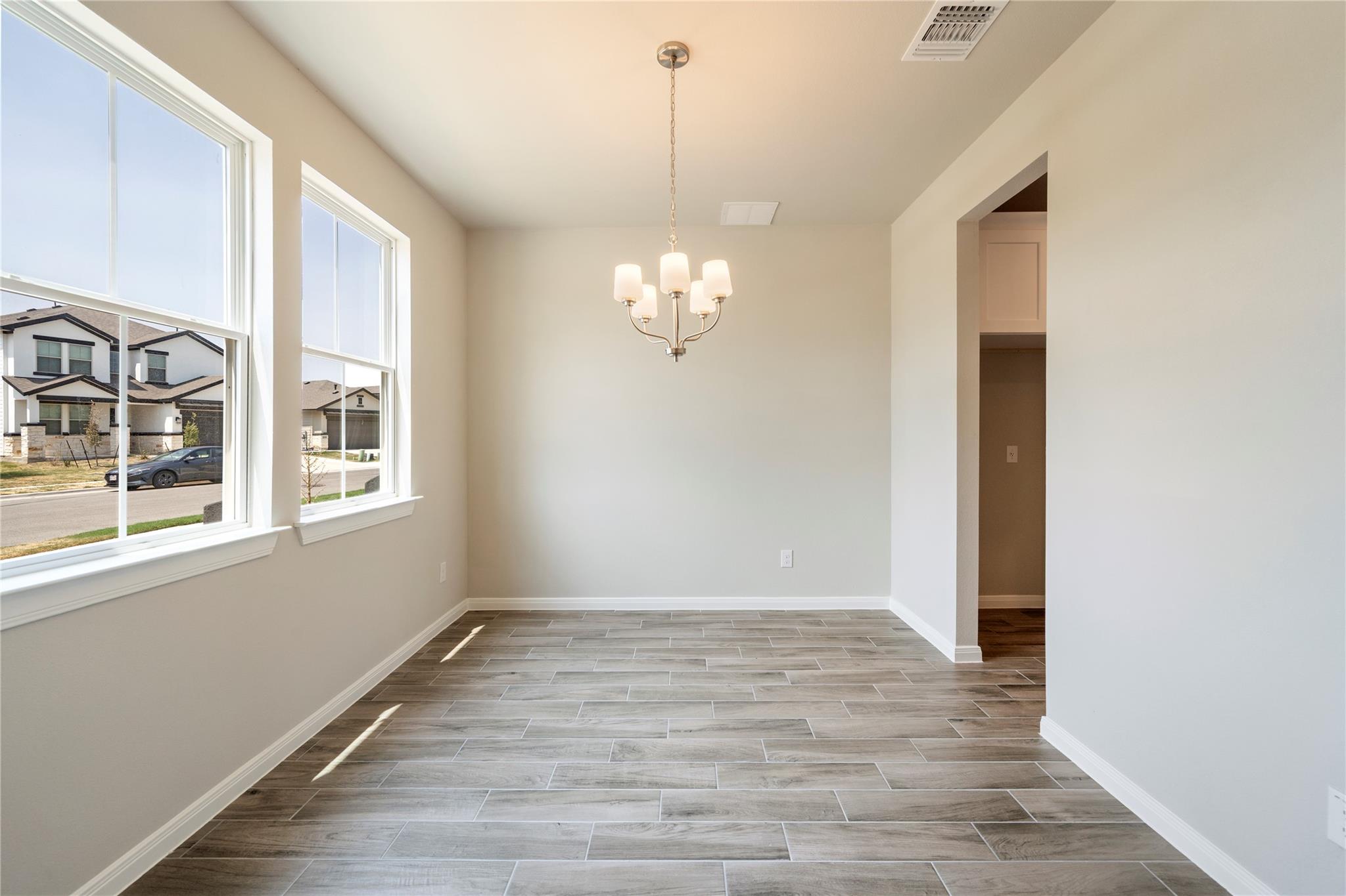 Empty dining room with gray tile flooring, large windows, and a chandelier.