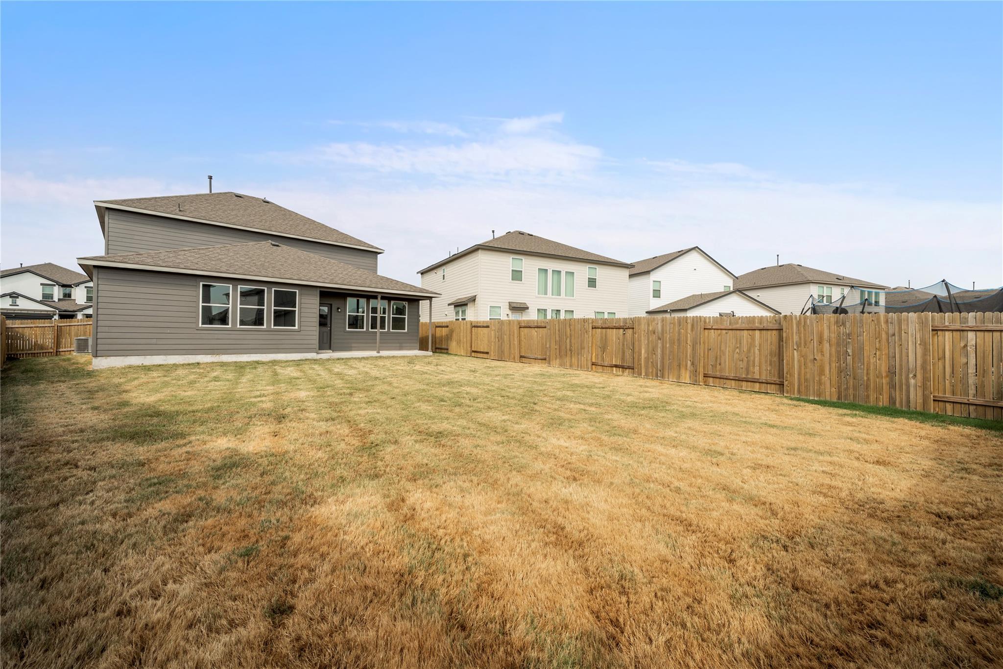 Home’s gray rear exterior and covered patio behind a broad lawn and wooden privacy fence.
