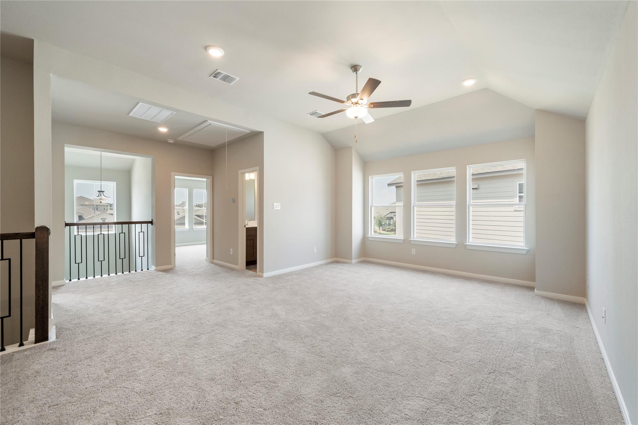 Empty upstairs bonus room with carpet, three windows, a ceiling fan, and stairwell railing.