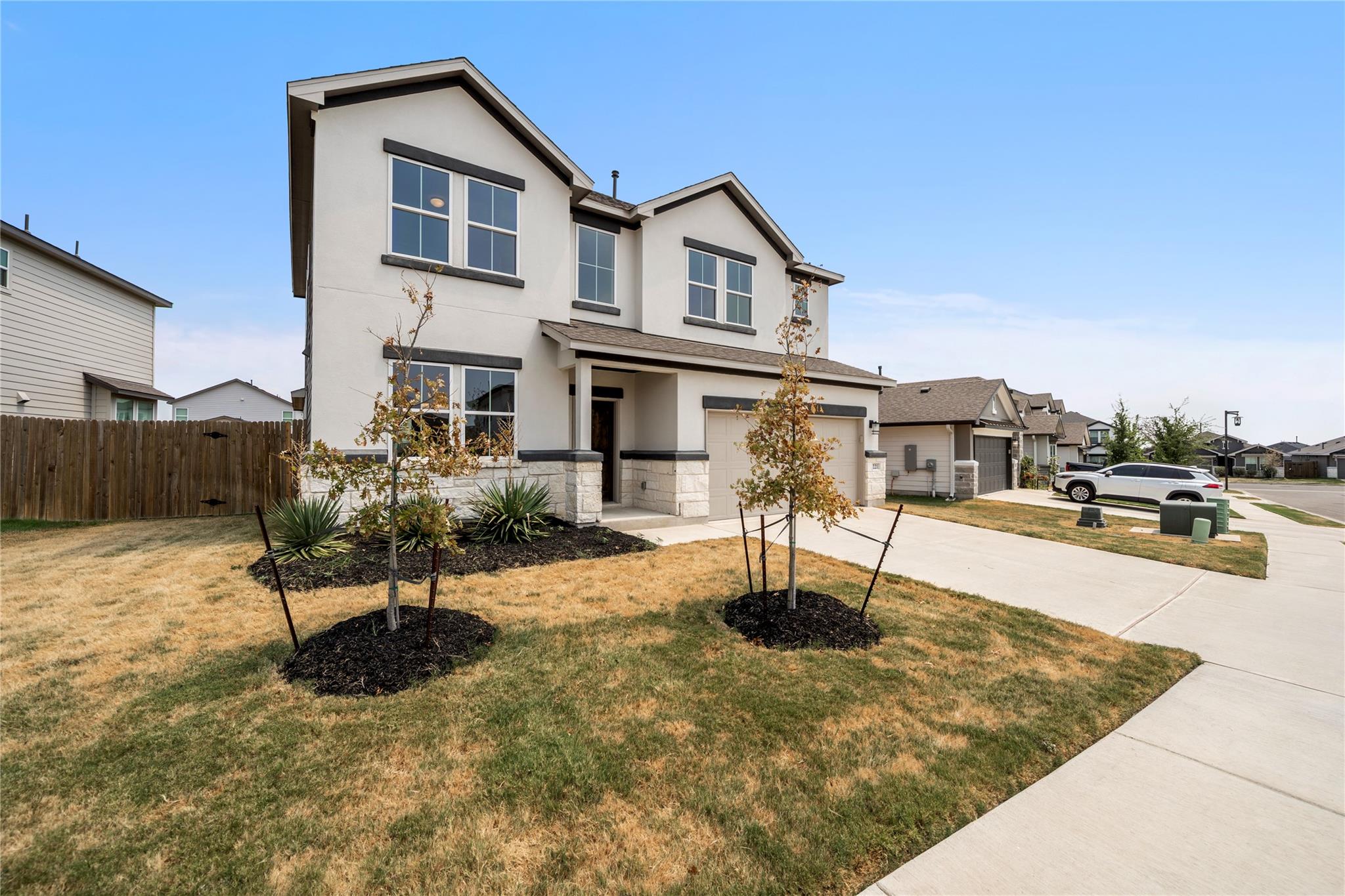 Two-story white house with dark trim, stone accents, an attached garage, and young trees in the front yard.