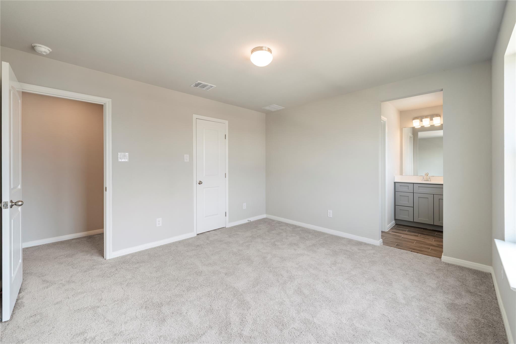 Unfurnished carpeted bedroom with an adjoining bathroom and gray vanity.