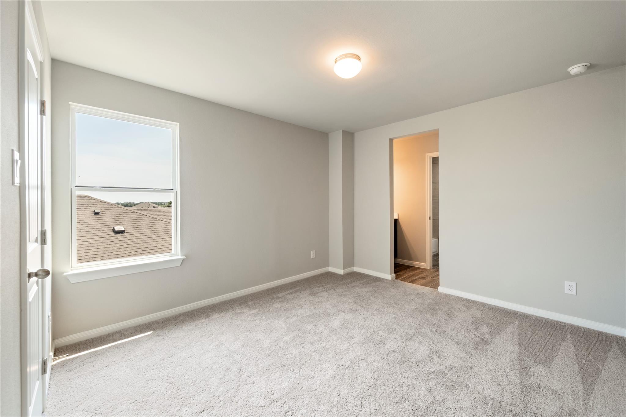Empty carpeted room with a large window and an open doorway to the hall.
