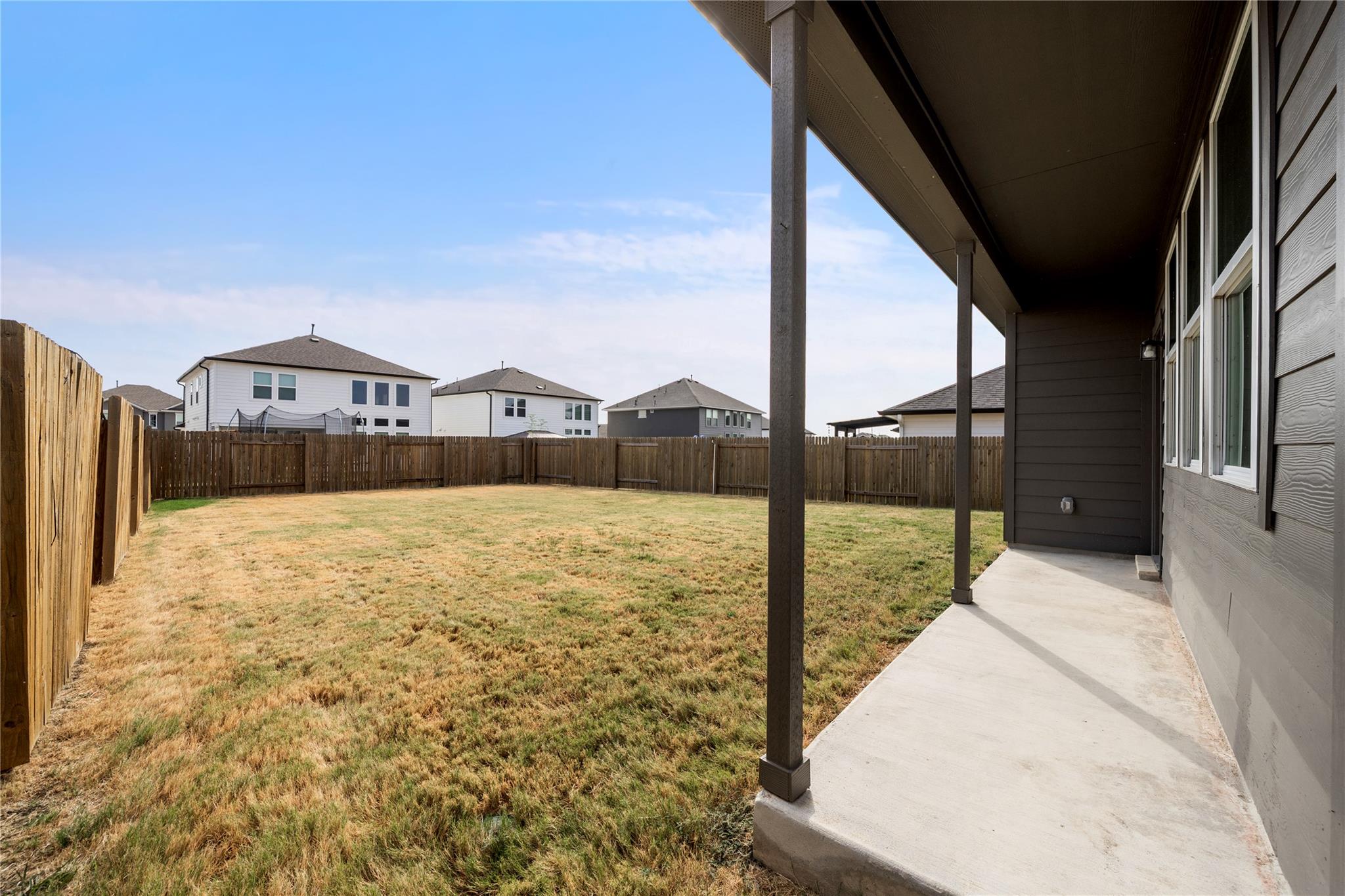 Fenced backyard with a covered concrete patio and broad lawn.