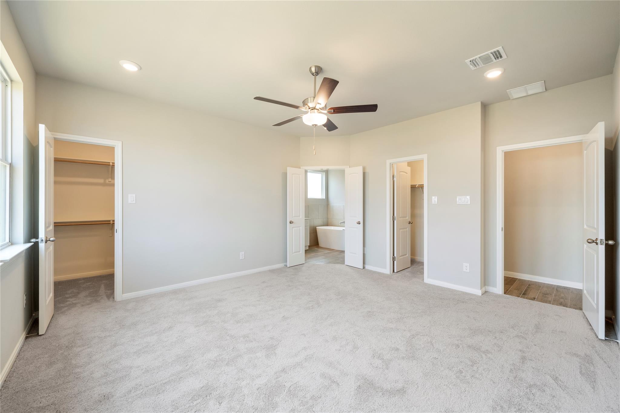 Vacant bedroom with gray carpet, a ceiling fan, and open doors to closets and a bathroom.