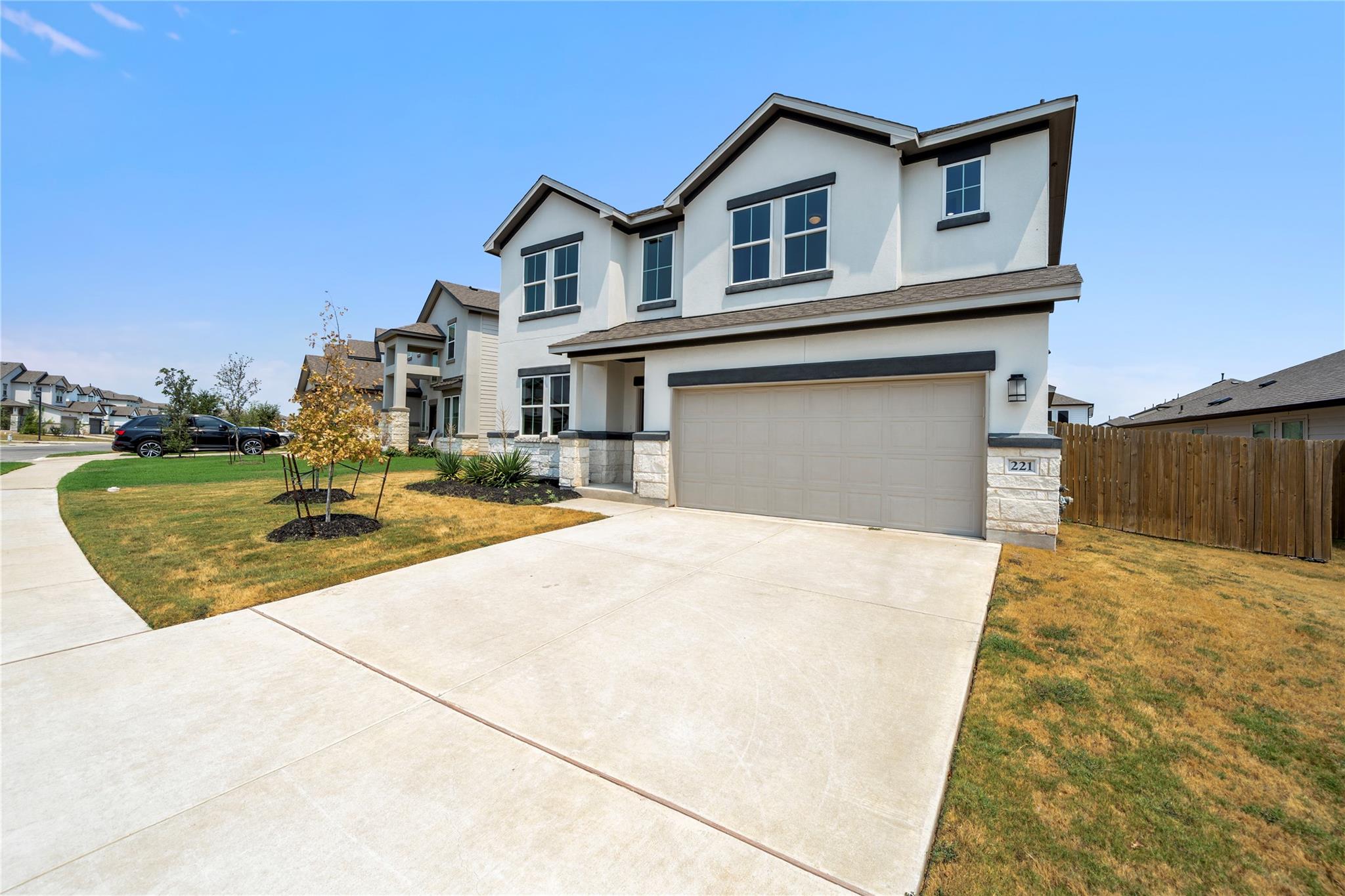 Two-story white house with dark trim, stone accents, and a wide driveway.