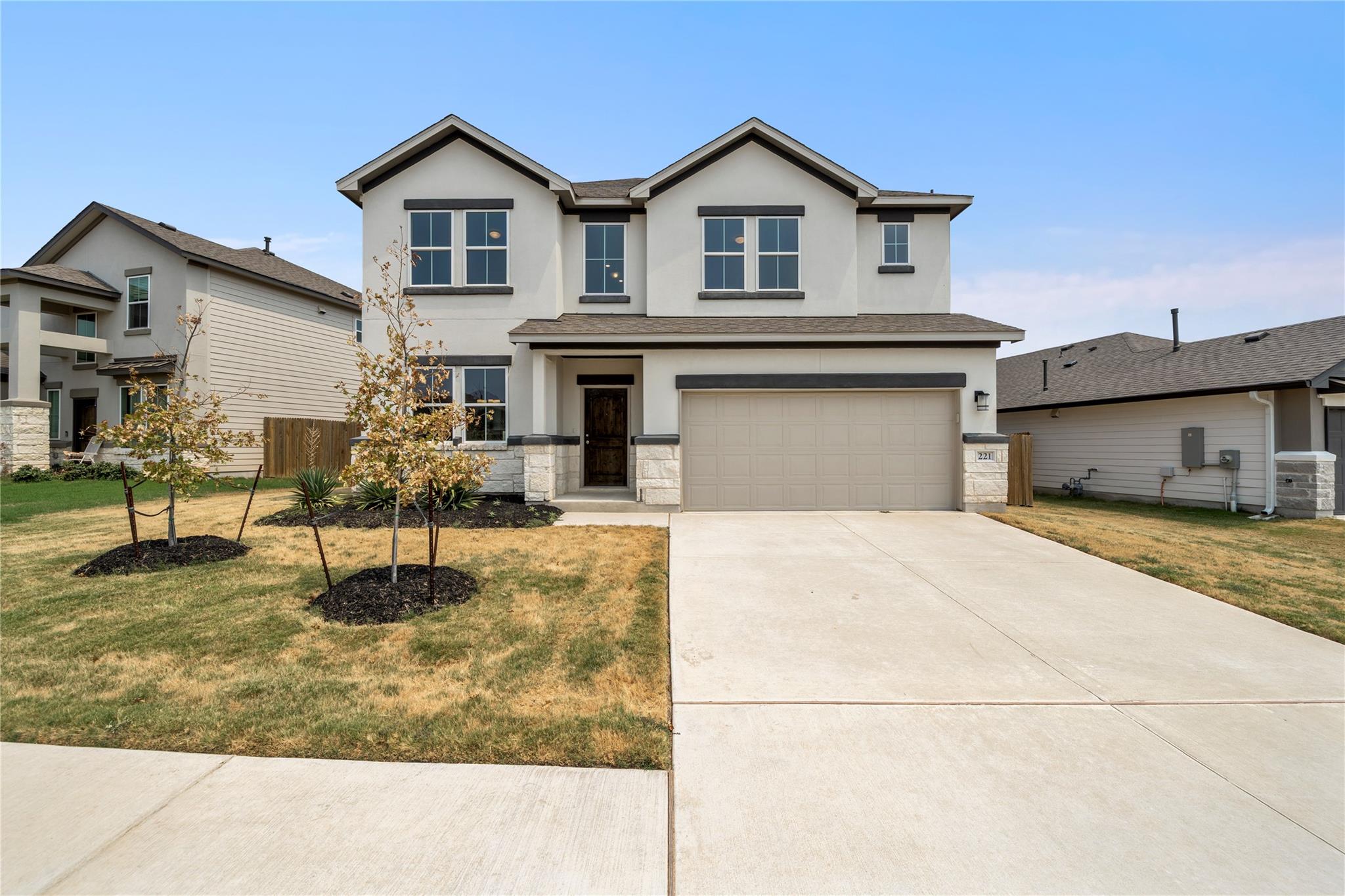 Two-story home with a double garage, concrete driveway, and young trees in the front lawn.