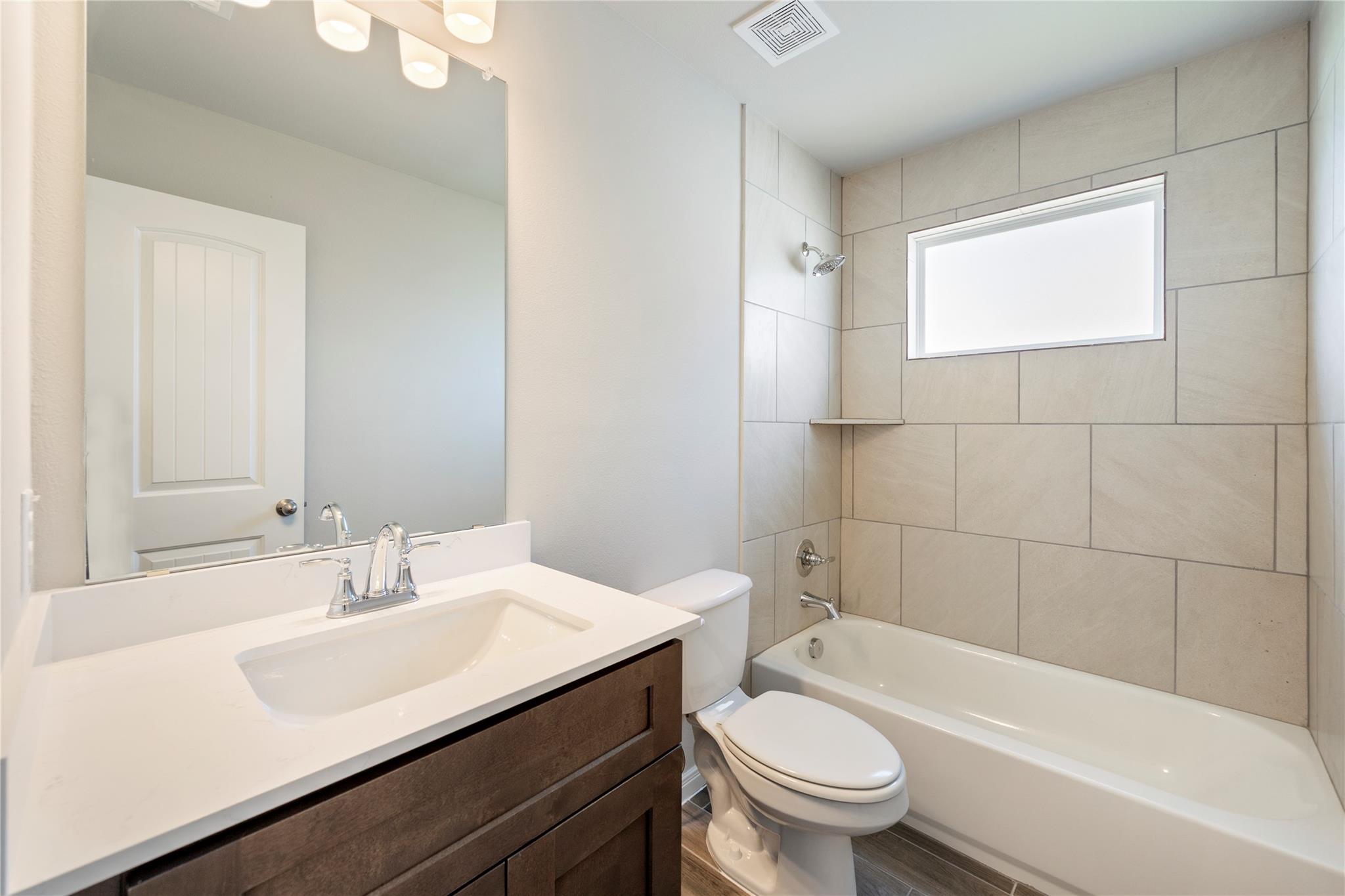 Bathroom with a dark wood vanity and a tiled bathtub beneath a high window.