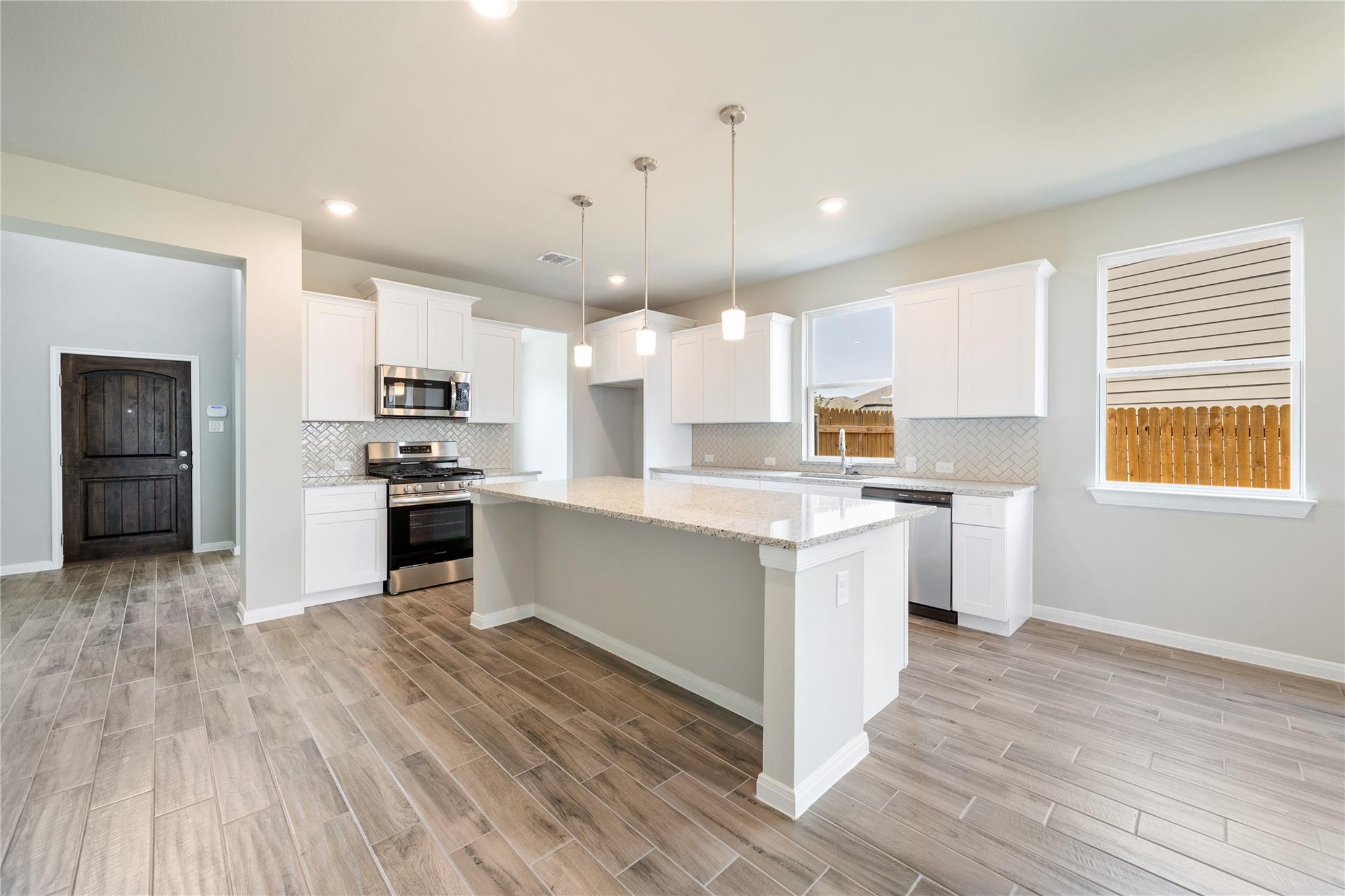 Kitchen with a large stone island, white cabinets, stainless steel appliances, and wood-look tile floors.