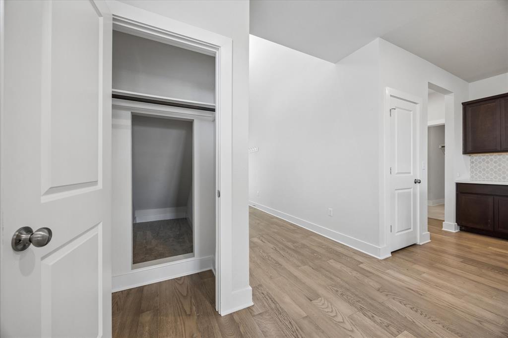 Open closet beside a room with light wood floors and dark kitchen cabinets.