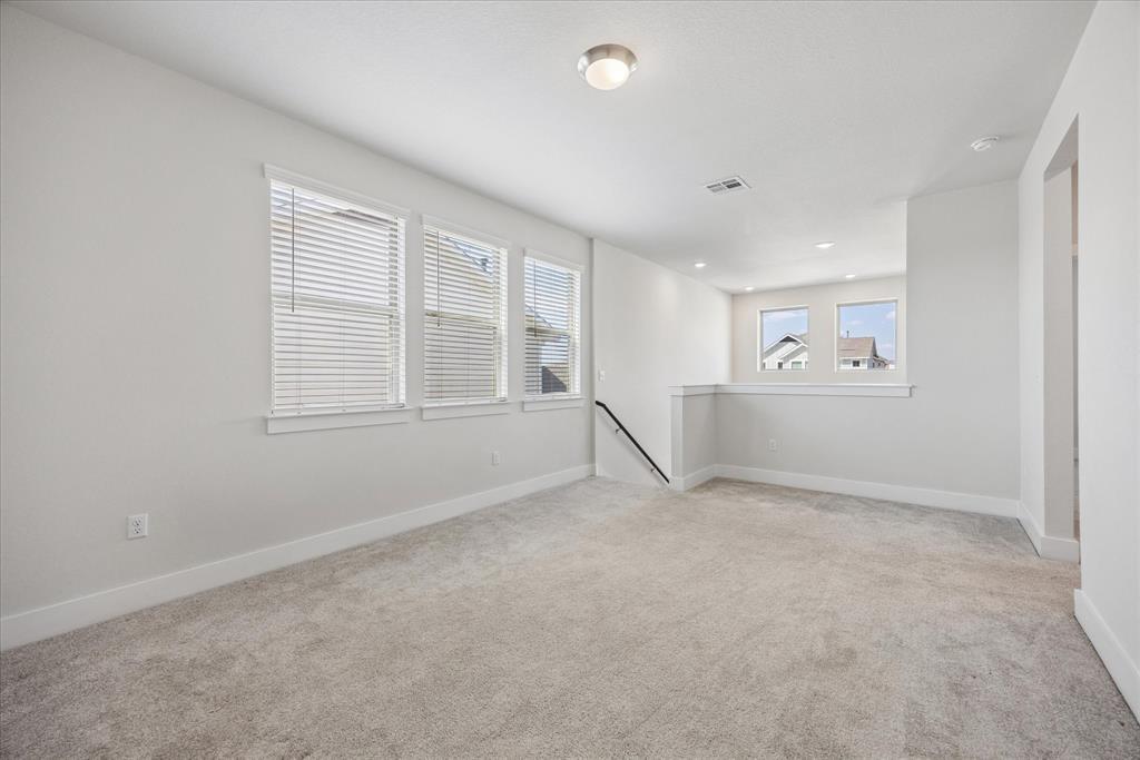 Empty carpeted upstairs living area with three blind-covered windows and a half wall by the stairs.