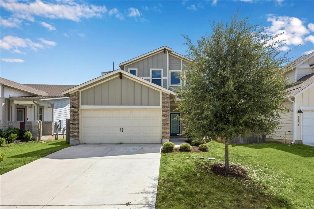 Two-story house with a double garage, brick accents, and a tree in the front yard.