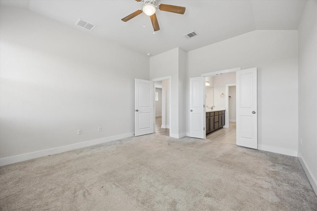 Empty carpeted bedroom with a wood-blade ceiling fan and open doors to an ensuite bathroom.