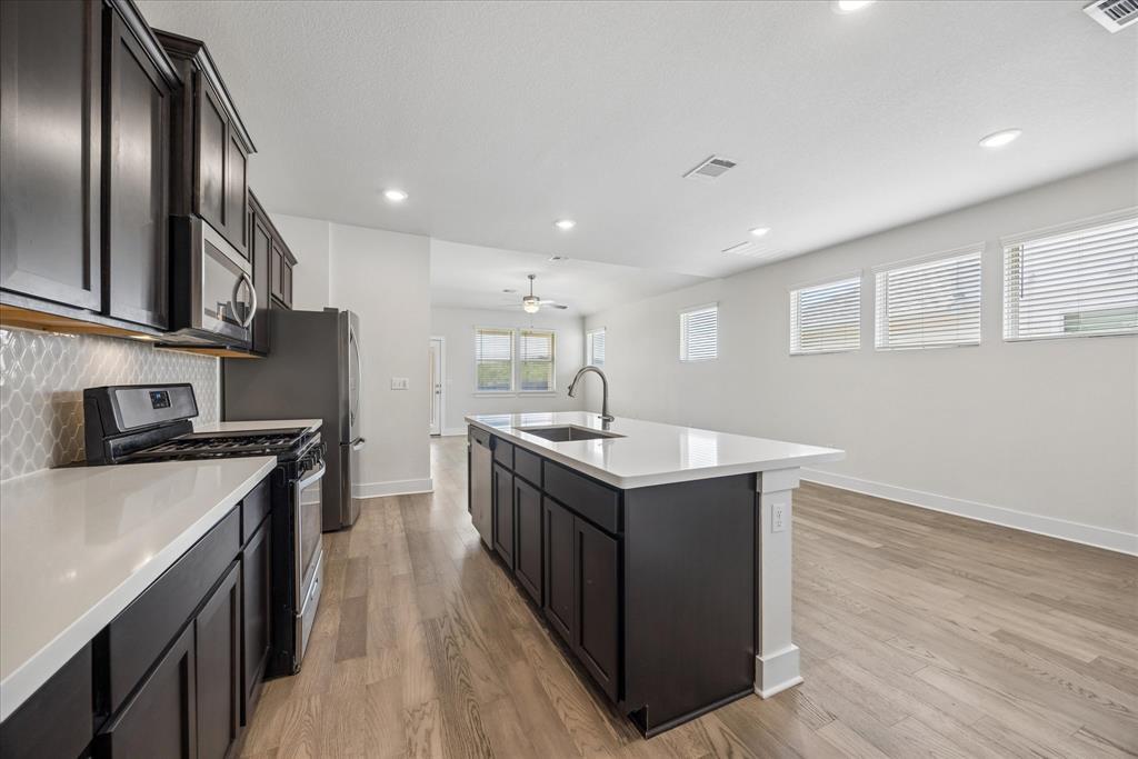 Kitchen with a large white island, dark cabinetry, stainless steel appliances, and light wood floors.