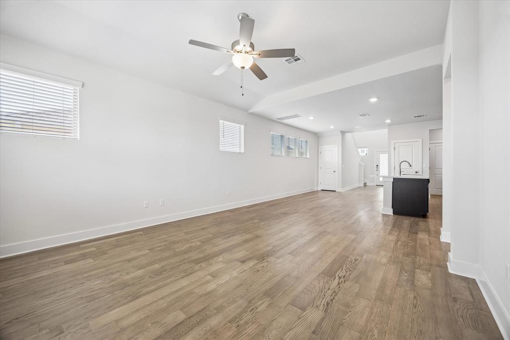 Open-plan living area with light wood floors, ceiling fan, and kitchen island.