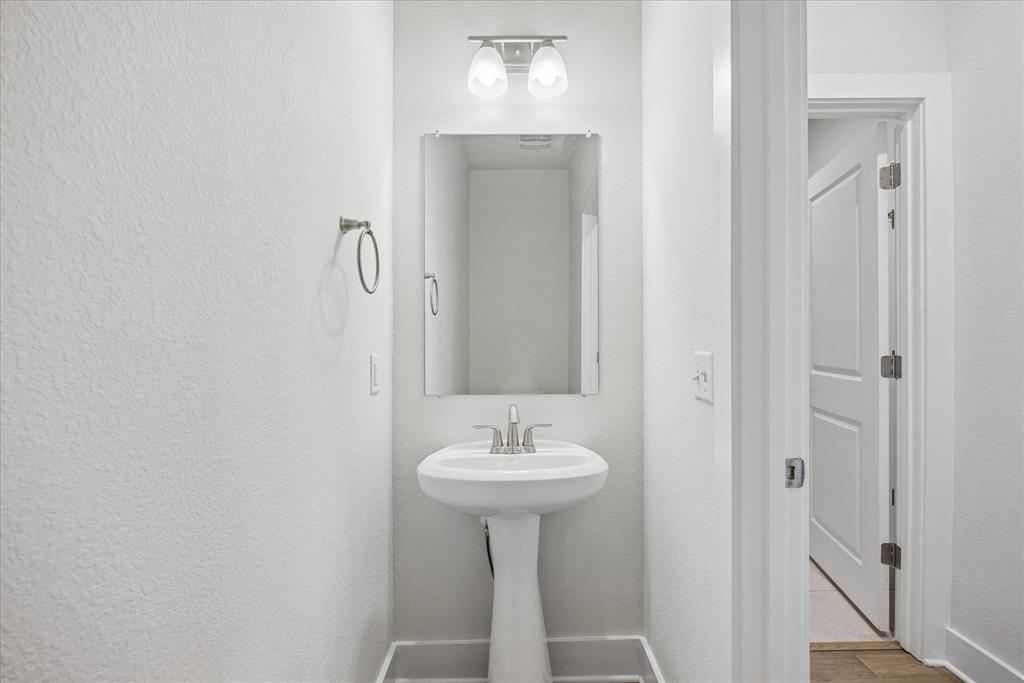 Bathroom with a white pedestal sink, rectangular mirror, and open doorway to the hall.