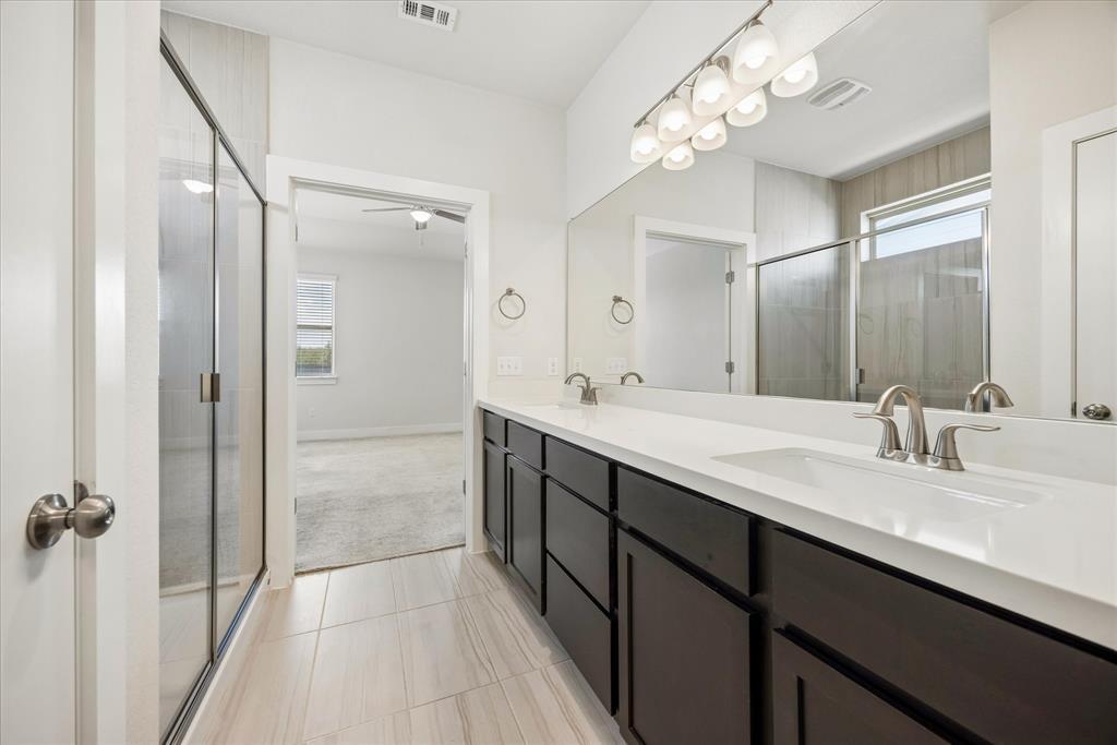 Bathroom with a double-sink vanity, dark cabinetry, and a glass-enclosed shower.