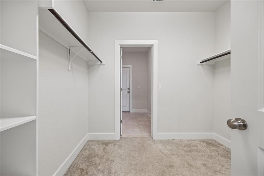 Empty walk-in closet with built-in shelves and hanging rods, opening onto a tiled hall.