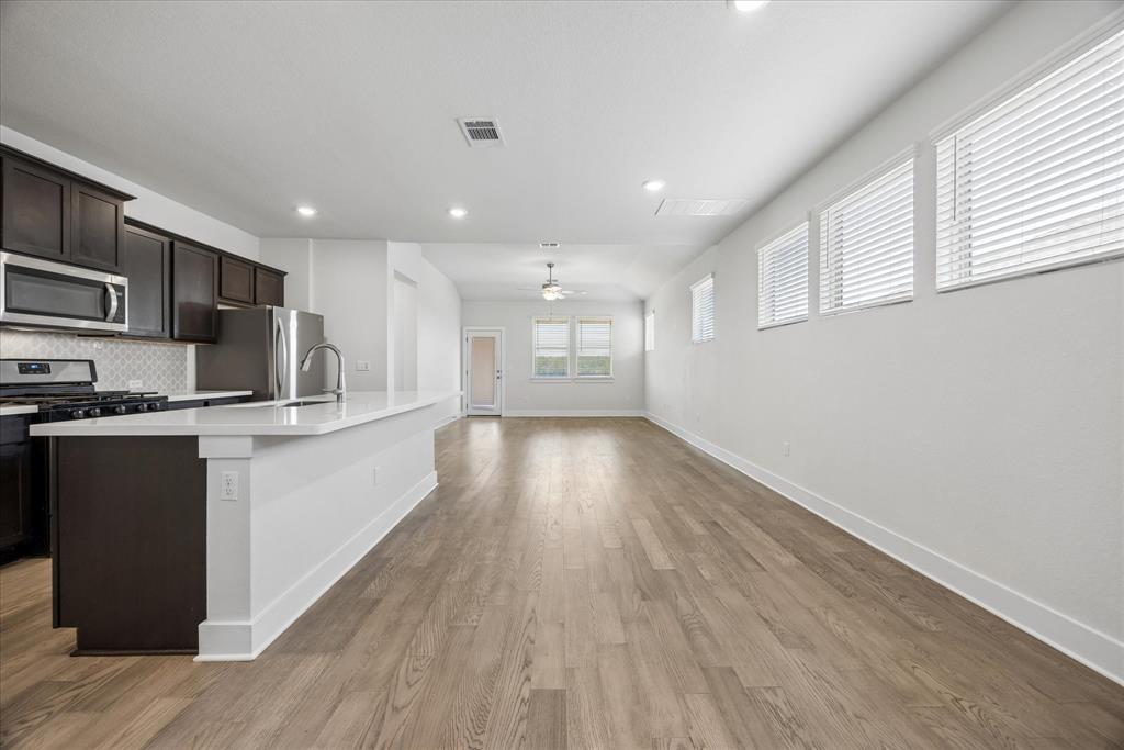 Open-plan kitchen and living area with dark cabinets, stainless steel appliances, and wood-look flooring.