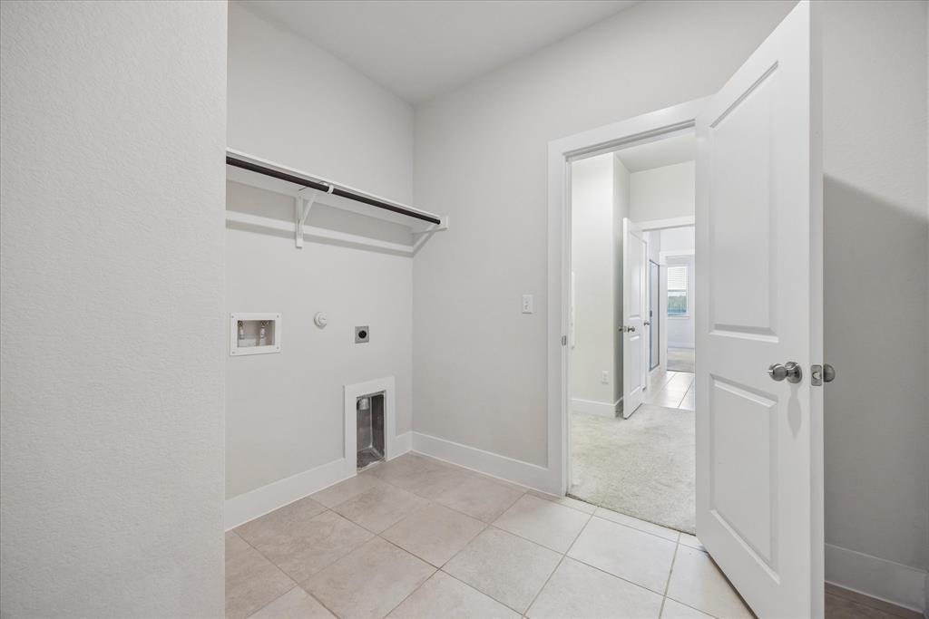 Empty laundry room with tile flooring, washer and dryer hookups, and a hanging shelf.