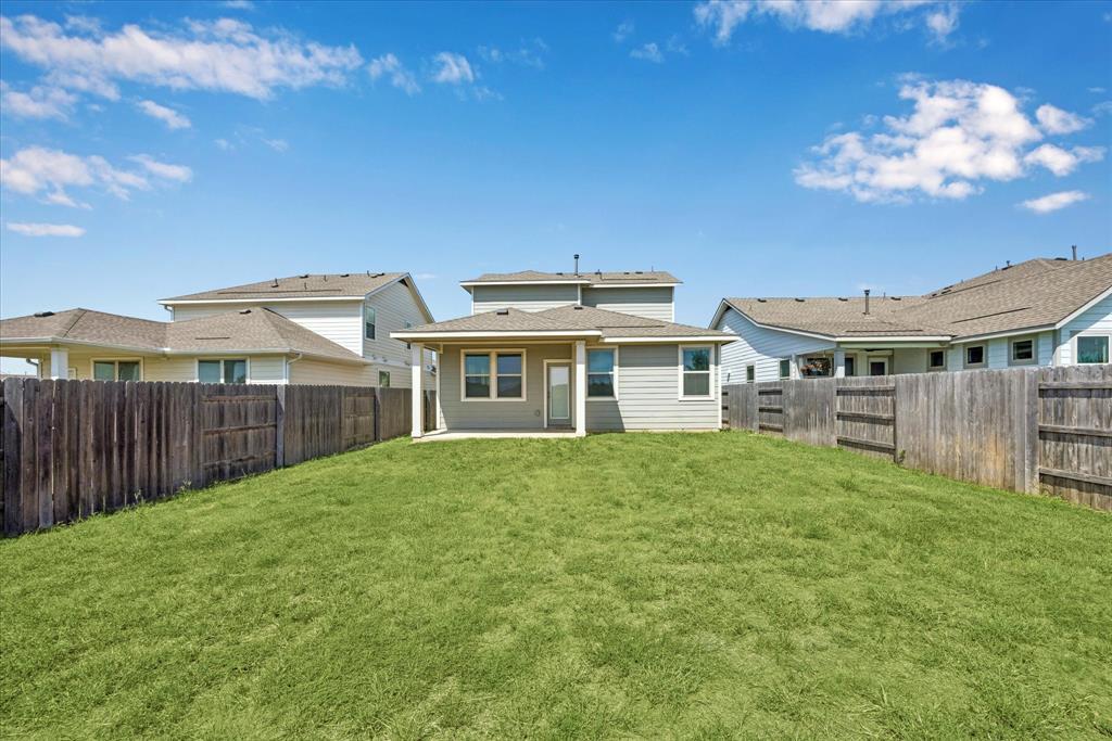 House’s rear exterior beyond a broad grassy backyard enclosed by wooden fences.