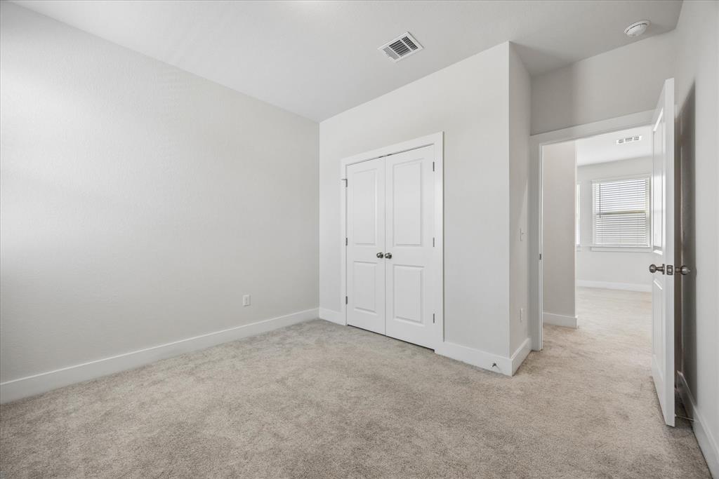 Empty bedroom with beige carpet, double-door closet, and an open doorway to a room with a window.