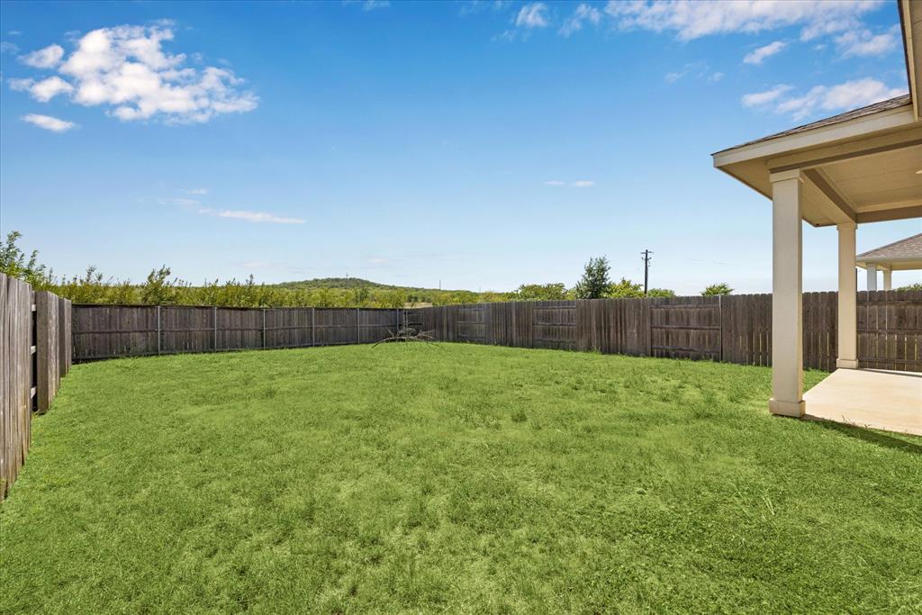 Fenced grassy backyard with a covered patio along the right side.