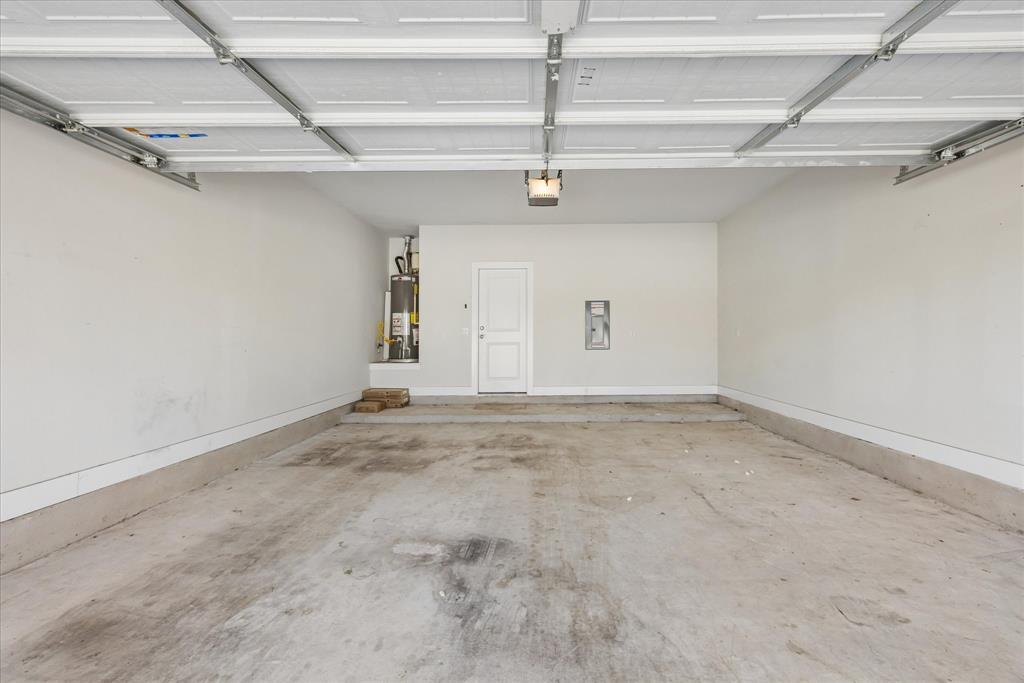 Empty garage with a raised overhead door, stained concrete floor, and water heater at the back.