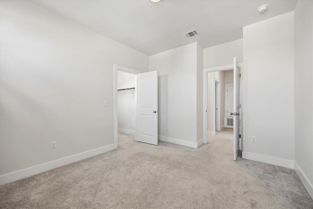 Empty bedroom with beige carpet, an open closet, and doors leading to the hallway.