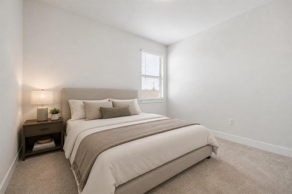 Staged bedroom with a neutral upholstered bed, beige bedding, and a window with blinds.