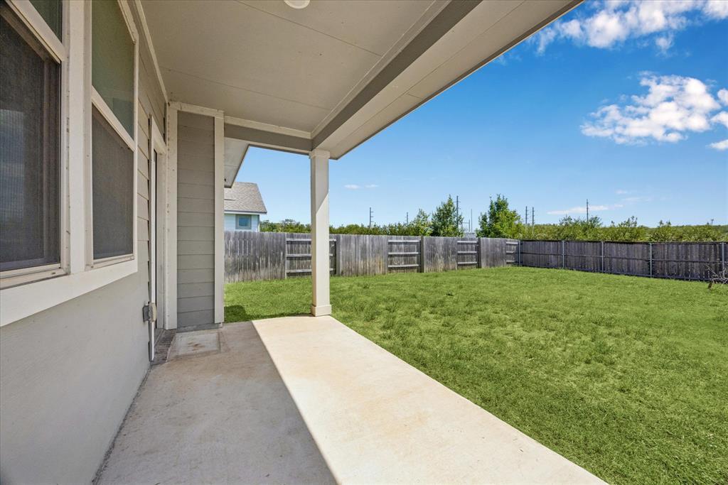 Covered patio overlooking a spacious grassy backyard enclosed by a wooden privacy fence.
