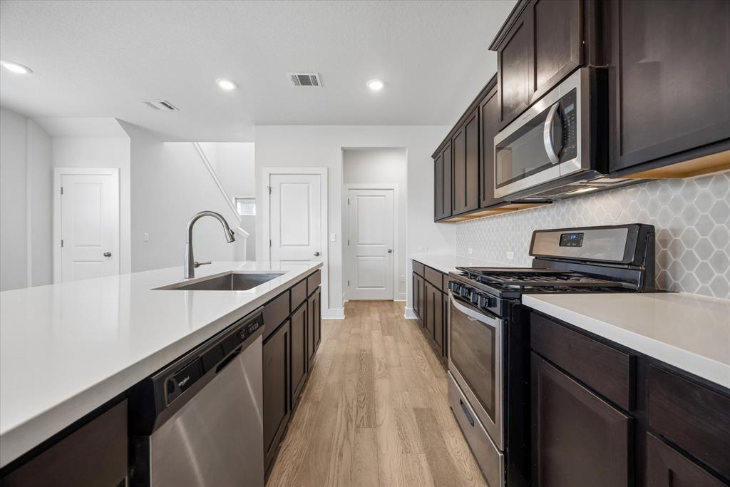 Kitchen with dark cabinets, white island, stainless steel appliances, and light hexagonal tile backsplash.