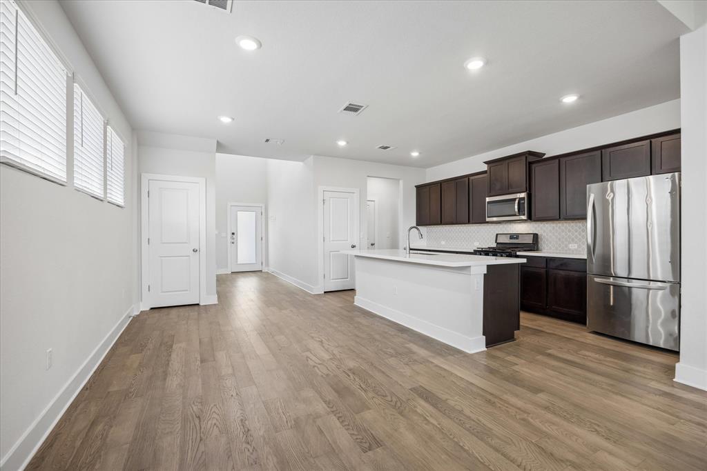 Open-plan kitchen with a white island, dark cabinets, stainless steel appliances, and light wood floors.
