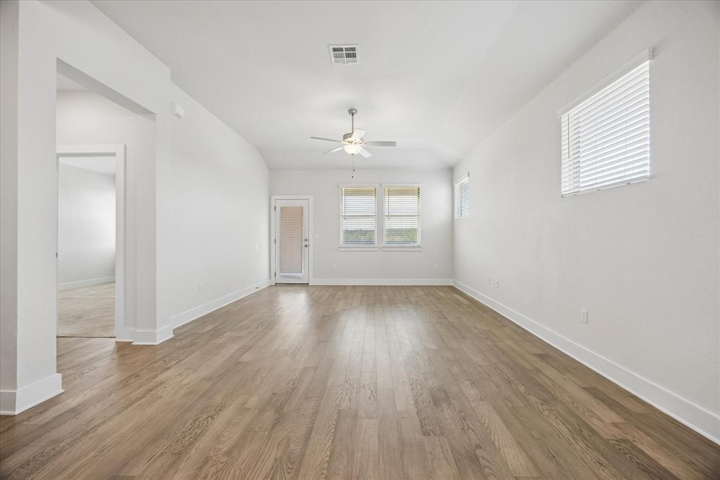 Empty living room with wood-look floors, a ceiling fan, and windows with blinds.