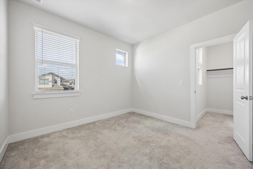Empty bedroom with beige carpet, a window with white blinds, and an open closet doorway.