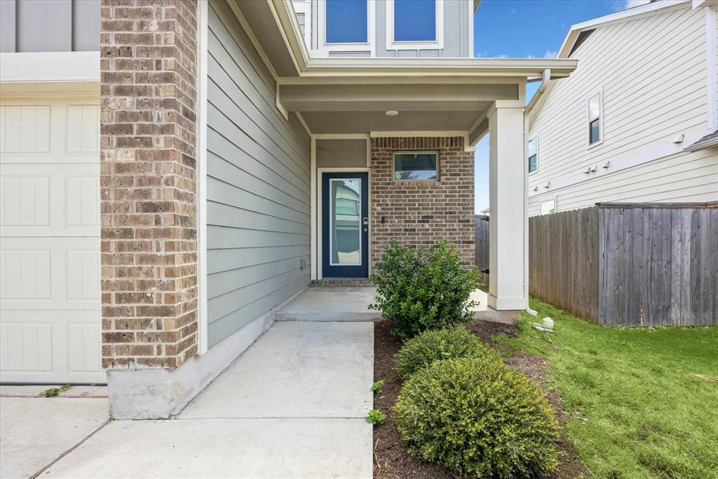 House entrance with a covered porch, blue door, brick accents, and landscaped walkway.