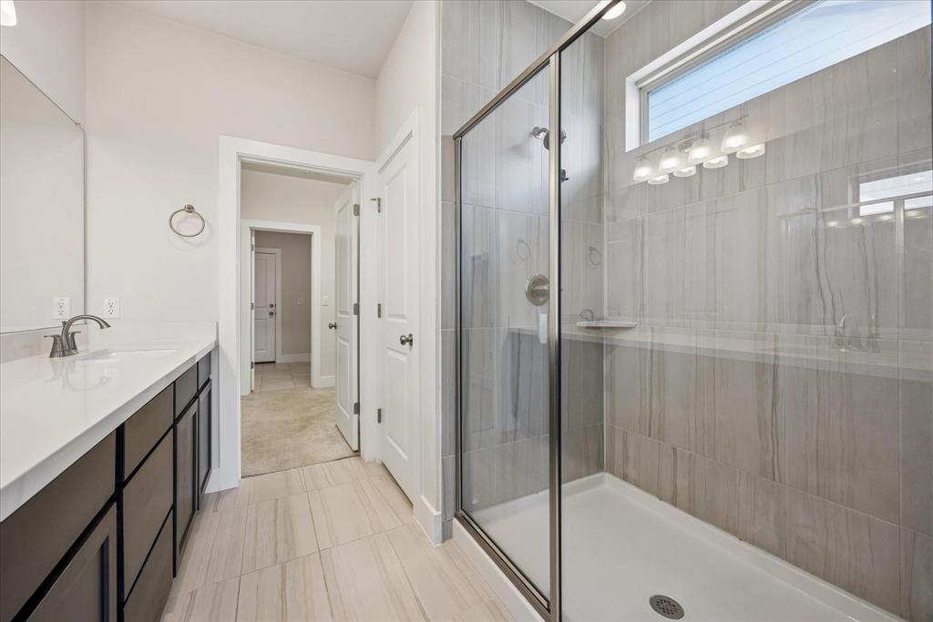 Bathroom with a dark double vanity and glass-enclosed tiled walk-in shower.