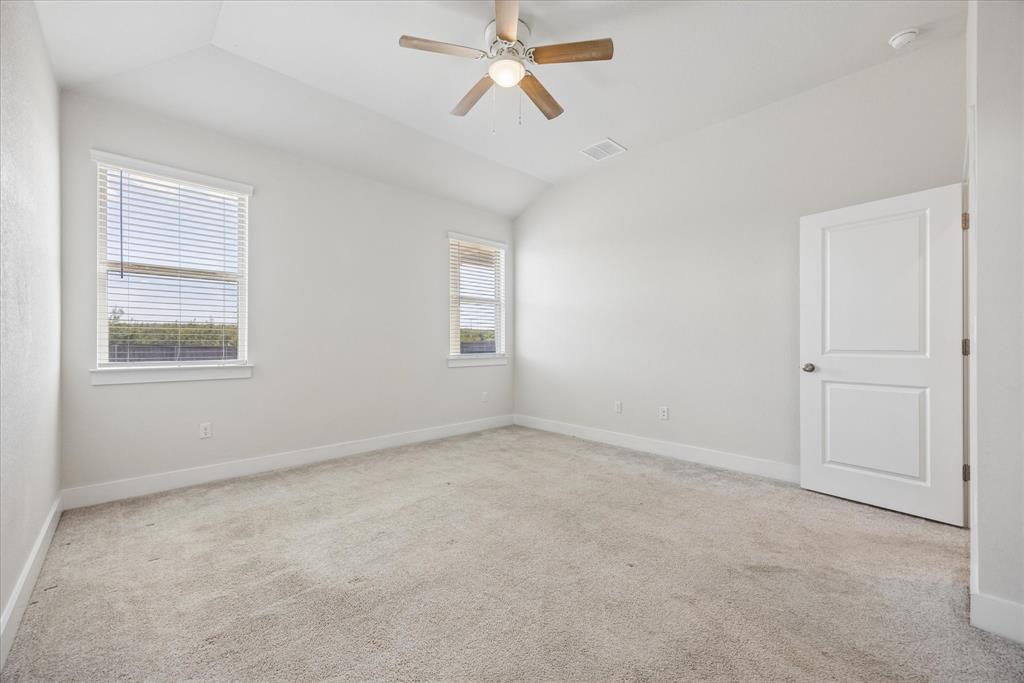 Vacant bedroom with beige carpet, two windows with blinds, and a ceiling fan.