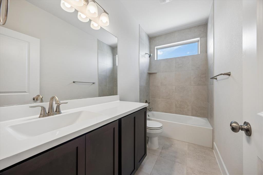 Bathroom with a long dark-cabinet vanity, tiled bathtub surround, and high narrow window.