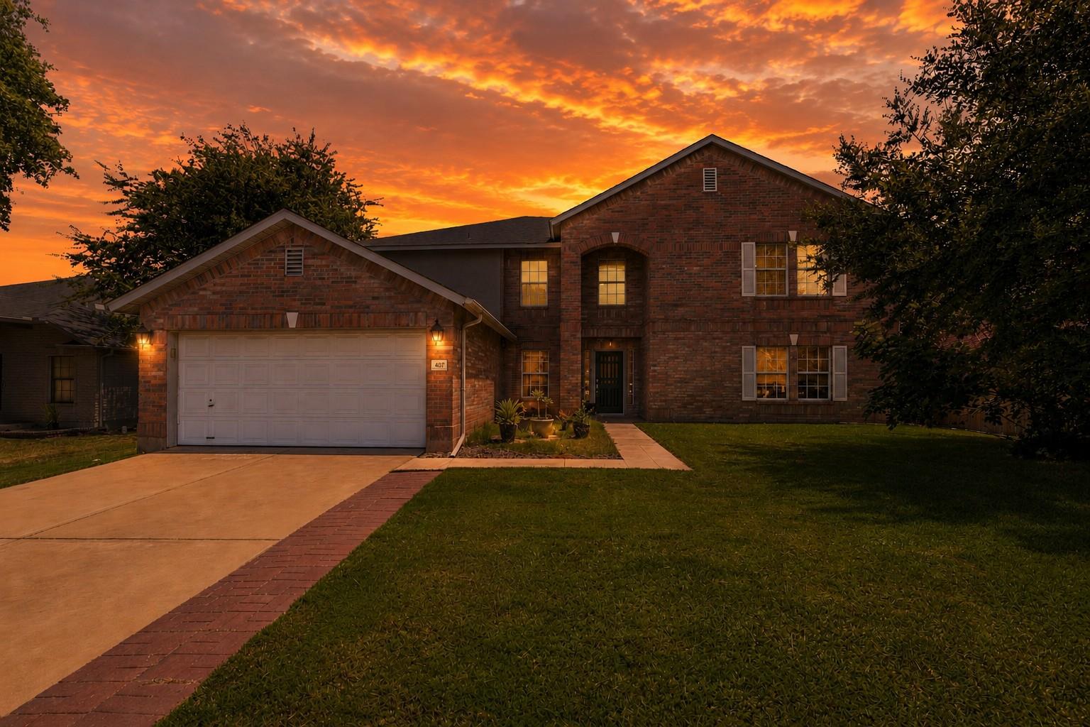 Two-story brick home with an attached garage and lit windows at sunset.