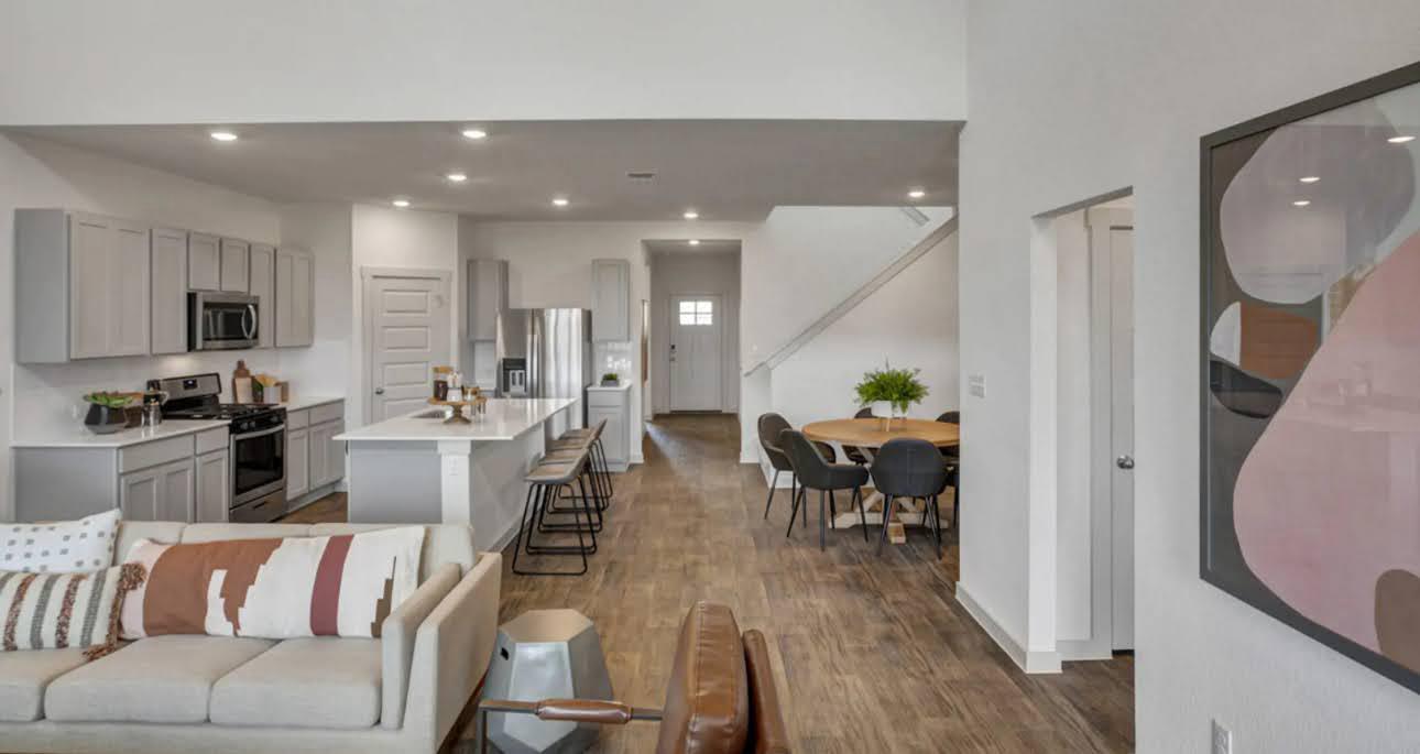 Open-plan kitchen and living area with a white island, stainless steel appliances, and wood-look floors.