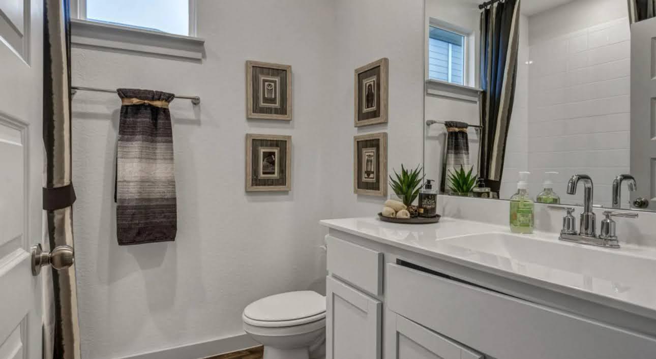Bathroom with a white vanity, chrome fixtures, toilet, framed art, and high windows.