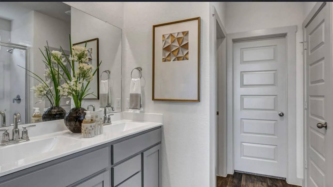 Bathroom with a gray vanity, white countertop, large mirror, and glass-enclosed shower.