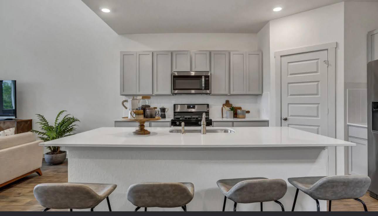 Kitchen with white cabinets, stainless appliances, and a large island lined with gray bar stools.