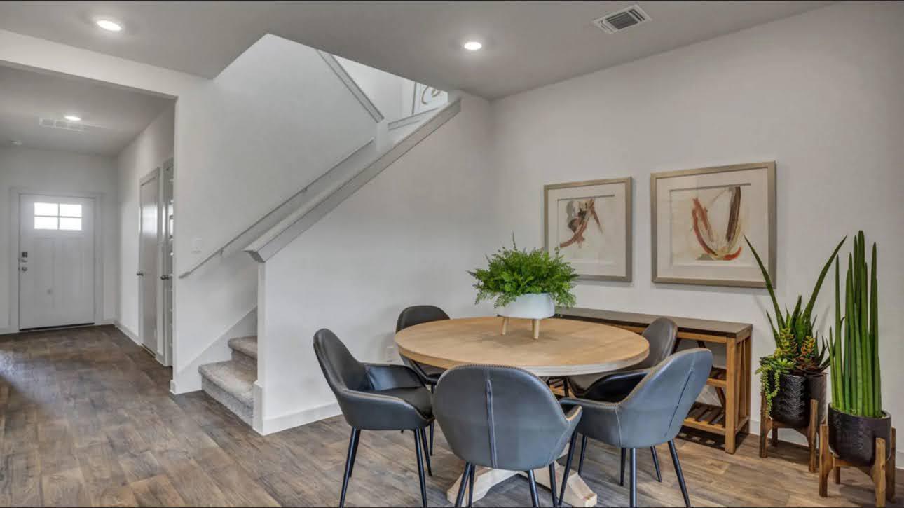 Dining area with a round wooden table, gray chairs, and a staircase beside the entryway.